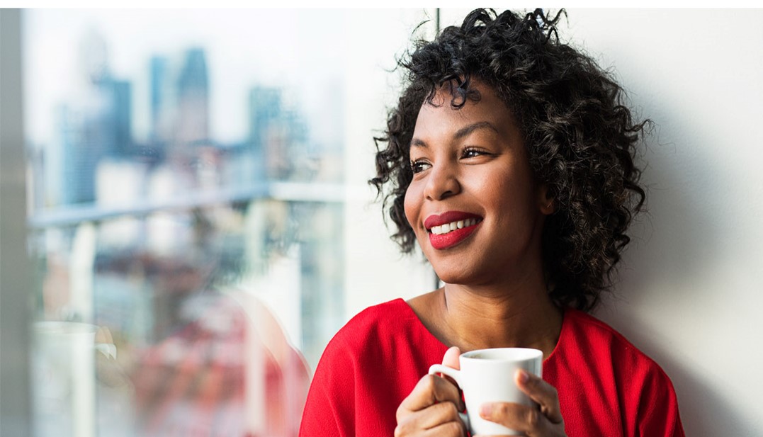 Mulher negra segurando uma caneca de café olhando pela janela 